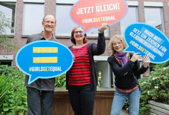 Das Team AG-Koordination: H. Ludwig, M. Sußner, W. Tebbe (v.l.n.r.) mit Sprechblasen zu Girls Get Equal als Schild-Version