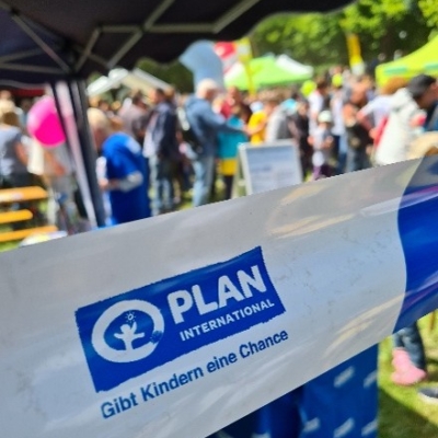 "Plan" Absperrband mit Logo vor Menschen