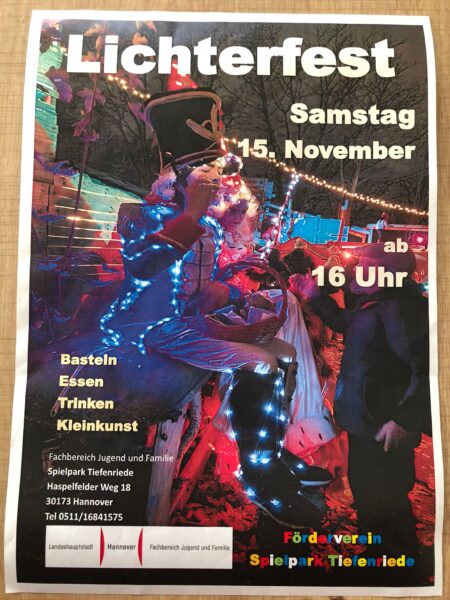 Ein farbenfrohes Plakat wirbt für das Lichterfest mit einem Darsteller in einem großen Hut, der von bunten Lichtern angestrahlt wird. Die Veranstaltung findet am Samstag, den 15. November, ab 16:00 Uhr mit Kunsthandwerk, Essen, Trinken und Kunst im Spielpark Tiefenriede in Hannover statt. Kontaktinformationen sind unten aufgeführt.