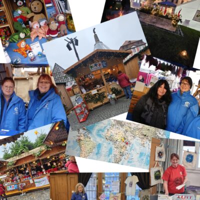 Eine Fotocollage von einem festlichen Markt im Freien: Menschen in blauen Jacken, handgefertigtes Kunsthandwerk, ausgestopfte Tiere, dekorierte Stände, eine Weltkarte und ein historisches Gebäude in der Abenddämmerung. Lächelnde Verkäufer und bunte Waren schaffen eine fröhliche, gemeinschaftliche Atmosphäre.