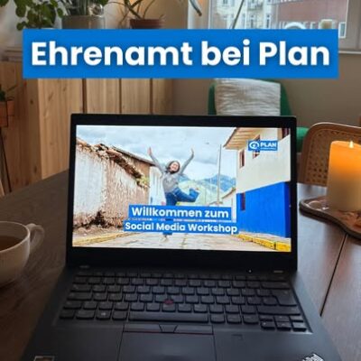 Ein Laptop auf einem Tisch zeigt das Bild einer lächelnden Person mit erhobenen Armen im Freien und dem Text Willkommen zum Social Media Workshop. Über dem Laptop steht in fetter Schrift "Ehrenamt bei Plan". In der Nähe stehen eine Kerze, eine Tasse und Pflanzen.