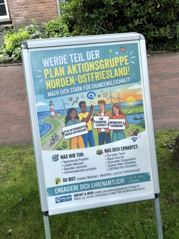 Ein Plakat im Außenbereich wirbt für die „Plan Aktionsgruppe Norden-Ostfriesland“. Darauf sind drei junge Menschen unterschiedlicher Herkunft abgebildet, die Protestschilder hochhalten. Der Text hebt das ehrenamtliche Engagement für den Wandel hervor und beschreibt Aktivitäten, Erwartungen sowie Kontaktdaten. Oben ziert eine Illustration einer Küstenstadt das Plakat.