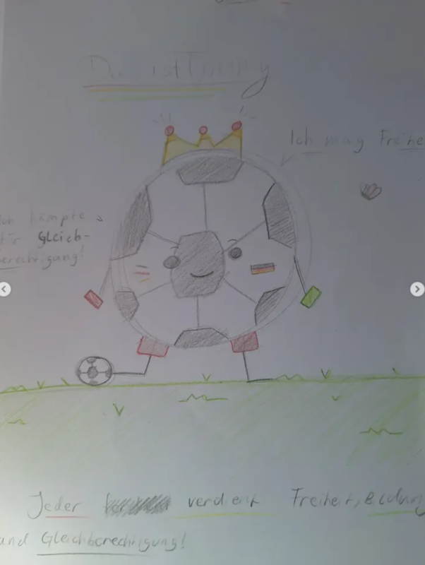 Ein handgezeichneter Fußball mit einer Krone, Augen, einem lächelnden Mund, Armen, die Fahnen halten, und Stangenbeinen steht auf einer Wiese. Ein kleiner Fußball liegt in der Nähe. Er ist von deutschem Text umgeben, darunter "Ich mag Freiheit" und "Jeder verdient Freiheit und Gleichberechtigung!".
