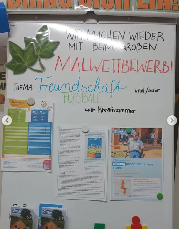 Ein mit zwei Papierblättern verziertes Whiteboard kündigt einen großen Malwettbewerb zum Thema Freundschaft und Fußball an. Unter der Ankündigung sind bunte Flugblätter, Wettbewerbsdetails und Informationsblätter angebracht.