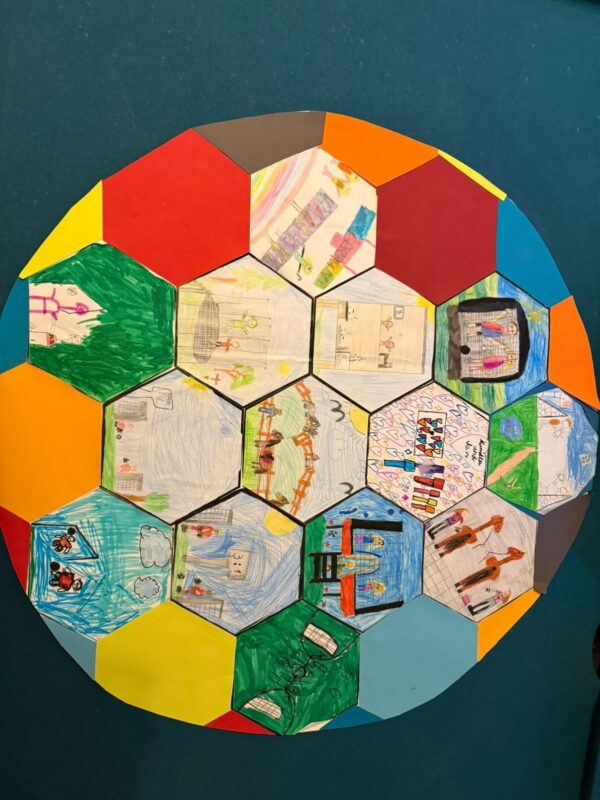 Eine große sechseckige Collage zeigt farbenfrohe Sechsecke, einige einfarbig und einige mit Kinderzeichnungen. Die Zeichnungen zeigen Häuser, Menschen, Spielplätze und Szenen aus dem täglichen Leben, die alle mit Filzstift umrissen und mit Buntstiften koloriert sind und ein lebendiges, spielerisches Mosaik ergeben.