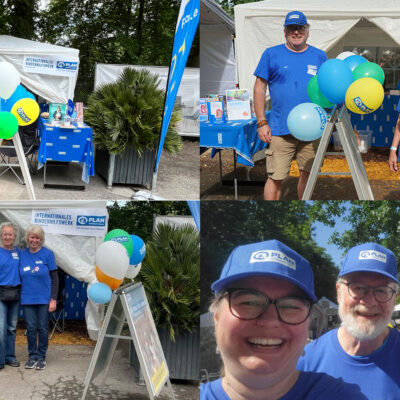 Eine Collage aus vier Fotos zeigt Menschen an einem Stand im Freien mit blauen „Plan International“-Schildern, Luftballons und einem Glücksrad. Freiwillige in blauen Hemden und Mützen lächeln in die Kamera oder stehen neben dem Stand, der von einem weißen Zelt überdacht ist.