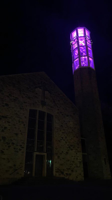 In der Nacht steht dort eine Steinkirche, deren hoher Glockenturm in helles violettes Licht getaucht ist. Die Kirche hat einen dunklen, gewölbten Eingang und ein in die Steinfassade eingemeißeltes Kreuz.