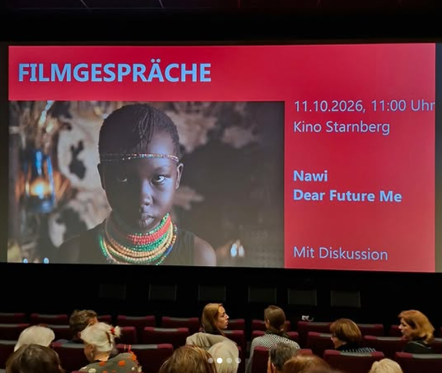 Auf einer Kinoleinwand ist ein Filmplakat zu sehen, auf dem ein junges Mädchen mit buntem Perlenschmuck abgebildet ist. Der Text auf der rechten Seite enthält Angaben zur Veranstaltung, darunter das Datum 11. Oktober 2026 und den Filmtitel Nawi: Dear Future Me.